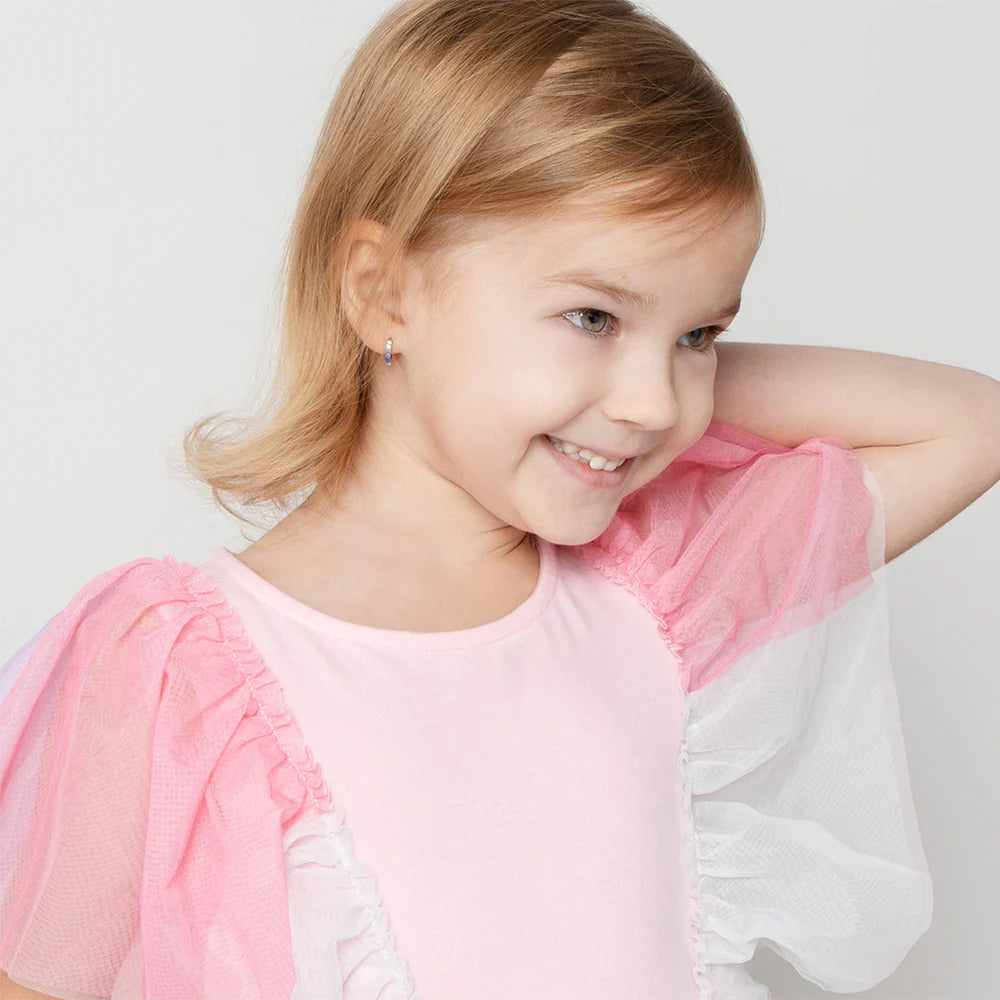 Children's earrings: Sterling silver paved CZ huggie hoops (blue) worn by a smiling girl in a pink outfit.