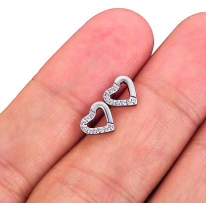 Heart-shaped silver earrings with clear stones held between fingers on a white background