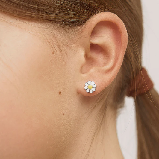 Close-up of an ear wearing a daisy flower earring with a blurred background