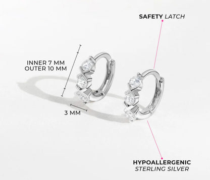 product infographic with size measurements of a pair of sterling silver huggie hoops with three white cubic zirconia separated by two silver X shapes. The earrings measure 7mm inner diameter, 10mm external diameter and 3mm width. 