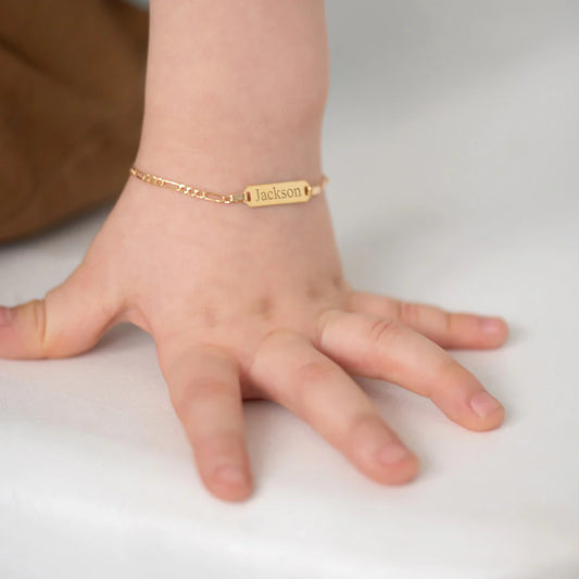 Figaro bracelet on child's wrist in 14k yellow gold with engraved identity tag, perfect for sensitive skin.
