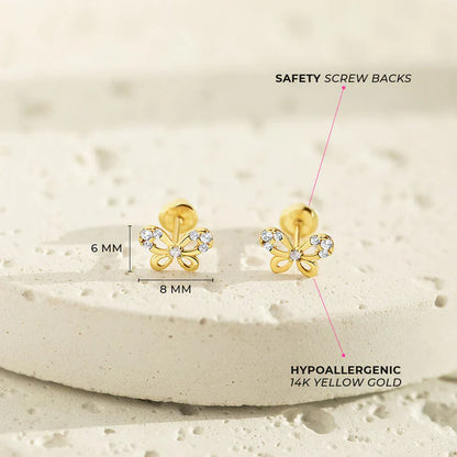 A pair of yellow gold butterfly shaped screw back earrings with clear cubic zirconia accents on a light porous stone surface