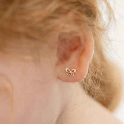 close up of a yellow gold butterfly earring in the lobe of a little girl's ear