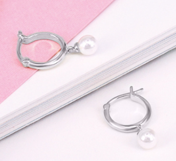 A pair of sterling silver snap back hoop earrings with white pearl adornments laid flat on a white and pink surface