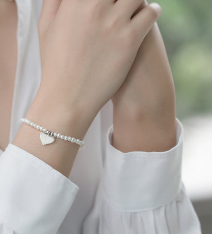 Freshwater pearl bracelet worn on a girl's wrist, featuring a sterling silver heart charm and delicate pearls.