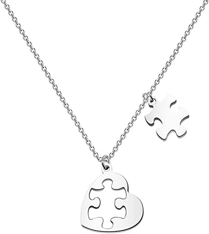 A polished silver necklace featuring a heart pendant with an integrated jigsaw piece cut-out, paired with a separate dangling puzzle piece charm, suspended from a fine silver chain against a white background