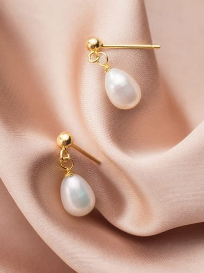 Pair of minimalist drop earrings on a pink cloth background, each featuring a polished gold ball stud connected by two small gold rings to a smooth teardrop-shaped white pearl.