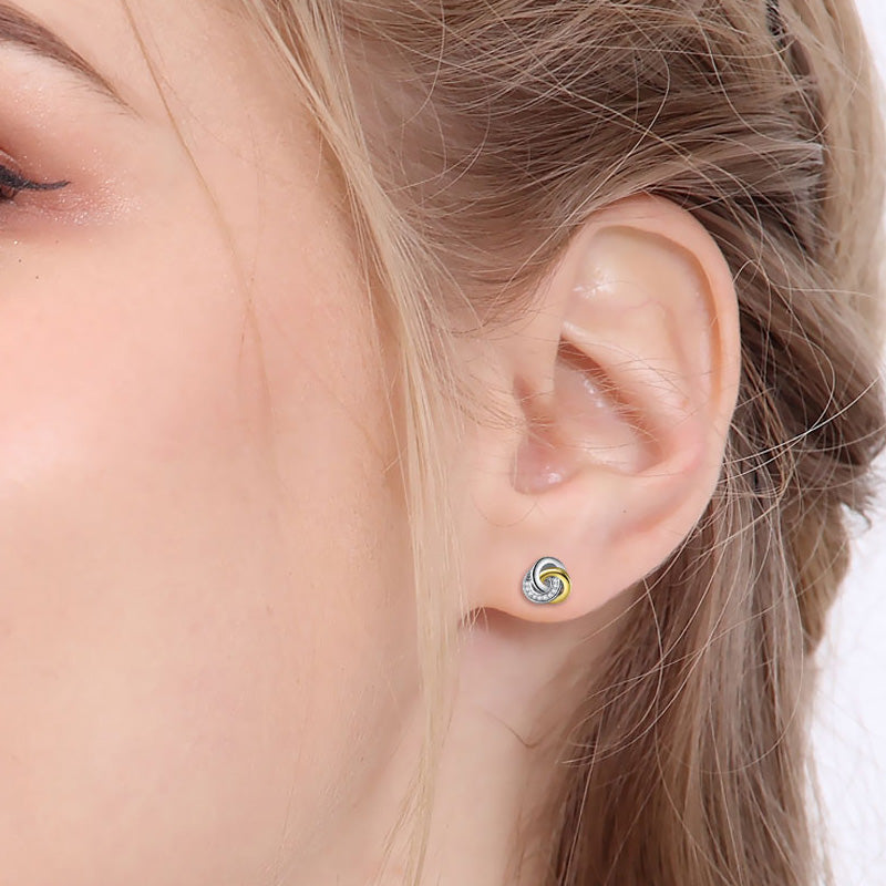 Endless knot earrings worn in a model's ear, showcasing 925 sterling silver and gold plating with cubic zirconia.