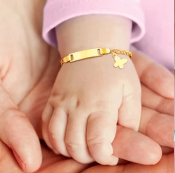 ID bracelet on a baby's wrist, featuring a butterfly charm and a gold finish, showcasing elegance and style.