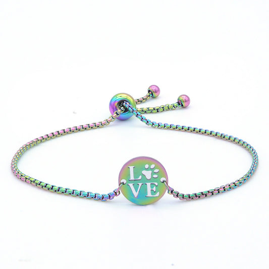Pet love bracelet in anodised steel with rainbow colors, featuring a round disc with cut-out 'love' and paw print.