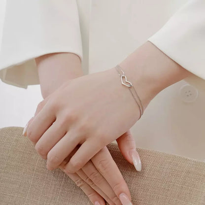 Sterling silver bracelet worn on a hand, featuring a delicate double chain and heart detail, perfect for teens and adults.