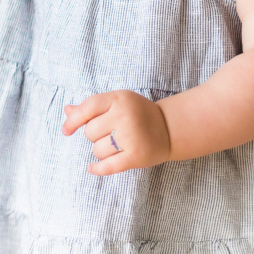 Child's hand wearing a sterling silver pink CZ heart ring, showcasing its delicate design and sparkling stones.