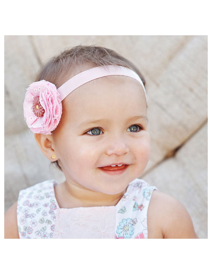Cute baby girl wearing a pink flower headband, showcasing joy and innocence in her smile.