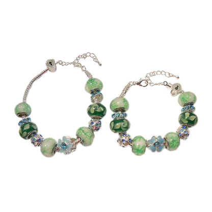A pair of European style baby/children's bracelets with a mix of blue, green, and white lampwork beads, silver plated spacers, and heart-shaped locket charms.