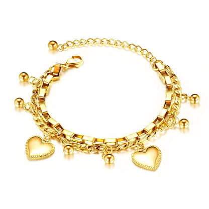 A gold-colored, double-layered children's bracelet with six balls and two heart charms, on a white background.