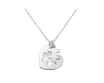 Sleek silver necklace with a heart-shaped pendant containing an interlocking puzzle piece cut-out, accompanied by a removable puzzle piece charm, displayed on a clean white background
