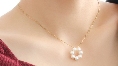 Gold necklace with a circular pendant made of white pearls, shown worn on a model with a red top.