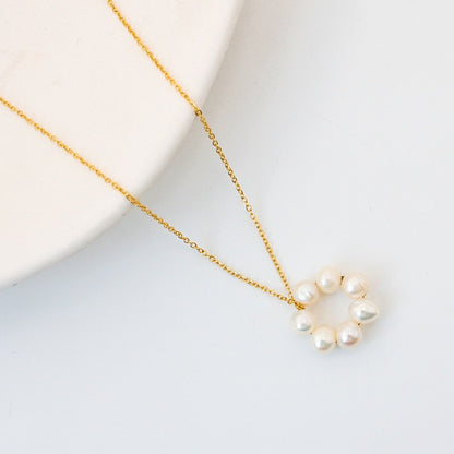 Gold necklace with a circular pendant of white pearls, laid flat on a white surface next to a round ceramic dish.