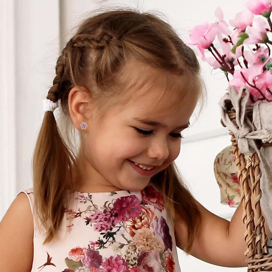 A little girl in a pink dress wearing a pair of silver flower shaped stud earrings with sparkling pink cz in her ears
