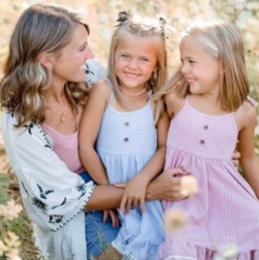 Mother and daughters enjoying a sunny day in floral dresses amidst nature.