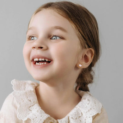 A little girl wearing a light coloured top with a lacey collar and tiny silver and pink enamel baby bird studs in her ears