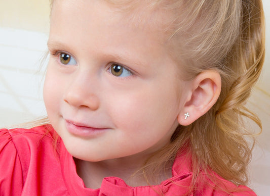 A young girl with blonde hair in a pink top with sterling silver cross earrings in her ears