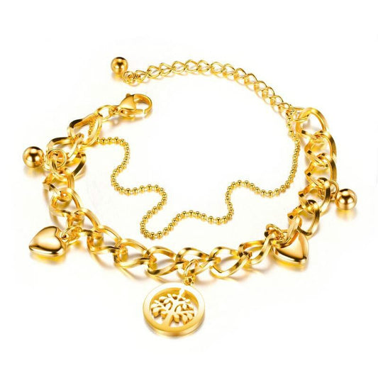 Two-layered gold-colored bracelet with chunky and fine strands, featuring a heart and a tree of life charm, on a white background.
